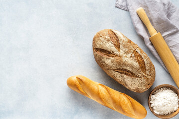 Homemade fresh bread with bowl of flour on stone background.