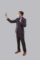 Obraz na płótnie Canvas Businessman Having Video Call on Phone Wearing Medical Mask Isolated. Indian Man Businessman Video Call. Business Online. Businessman Using Phone. Indian Business man Standing Full Length