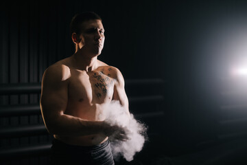 Strong muscular man clapping hands with talc before lifting barbell at the gym. Weightlifter preparing for fit workout in gym with chalk magnesium carbonate.