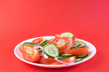 Simple vegetable salad of tomato, cucumber, onion and dill in white plate on bright red background. Copispace. The concept of vegetarianism, proper nutrition, organic products, vitamins, homemade food