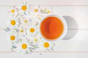 Fototapeta na wymiar Chamomile tea in a white little cup on a light wooden surface. Around the cup are scattered flowers. The concept of natural vitamin drinks for health, immunity. Top view, flat lay..