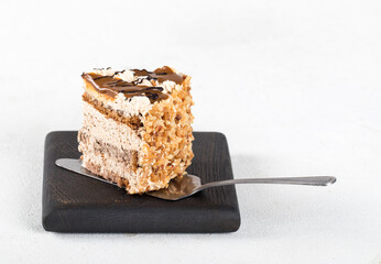 A piece of biscuit cake with cream, caramel, nuts and chocolate on a light background