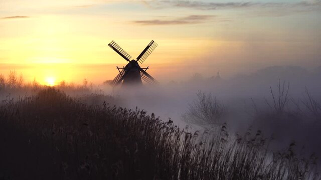 Sunrise with traditional, Dutch windmill and a canal in the spring fog.