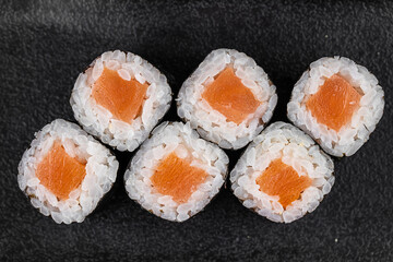 Maki Sushi Rolls with salmon on black stone on dark background. With ginger and wasabi. Sushi menu. Japanese food. Closeup of delicious japanese food with sushi roll. Horizontal photo