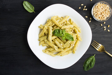Italian pasta with pesto and pine nuts in the white plate on the black wooden background. Top view. Copy space.