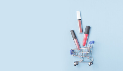 Women's lipsticks and lip glosses in a shopping trolley on a blue background. The concept of buying...