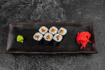 Sushi California Roll with crab meat, cucumber, masago, chopsticks on a gray plate, black background, side view
