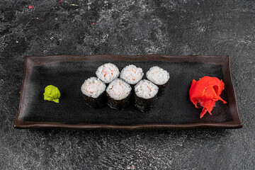 Obraz na płótnie Canvas Sushi California Roll with crab meat, cucumber, masago, chopsticks on a gray plate, black background, side view