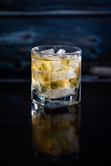 A full glass of whiskey with ice. Serious male drink. Rum in a glass on a blue background. Alcoholic beverage at the bar.
