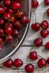 Scattered berries of ripe cherries on a light wooden background and in a bowl. Top view. Seasonal Vitamins. Vertical.