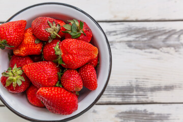 Berries of ripe red strawberries in a bowl on a light wooden background. Seasonal Vitamins. Close-up. Top view.
