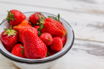 Berries of ripe red strawberries in a bowl on a light wooden background. Seasonal Vitamins. Close-up. Top view.
