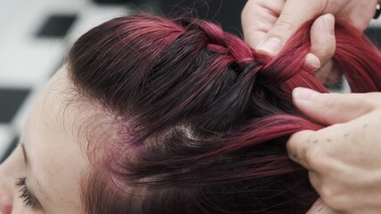 Professional hairdresser plaiting braids to red colored female hair
