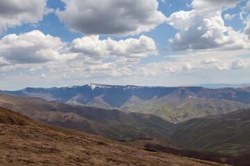 Panoramic view of amazing mountain layers lighten by soft light, fluffy white clouds on a blue sky and foreground saffron flowers