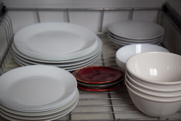 White porcelain dishes dried on metal dish rack. Way to organize kitchen and minimize space with modern drainer in cabinet against white background.