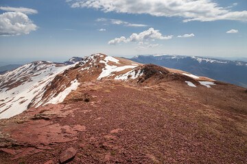 Beautiful view from a mountain peak covered by remaining snow at the end of winter and dark, red rocks at a rocky highlands and cliffs under a blue aky