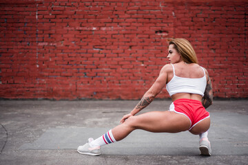 Young woman bodybuilder posing while standing with her back against a brick wall. Outdoor sports in isolation. A strong and muscular girl is engaged in fitness on a sports field.