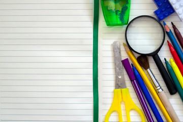 Back to school. Top view on a school desk with school subjects. Scissors, felt-tip pens, pencils, magnifying glass, open writing paper. Copy space