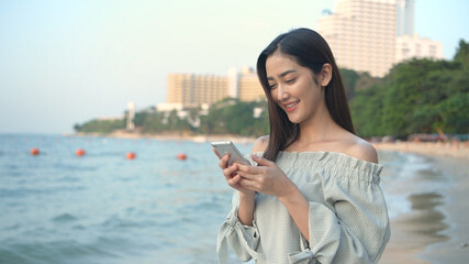 Holiday concept. An Asian woman is playing cell phones on the beach. 4k Resolution.