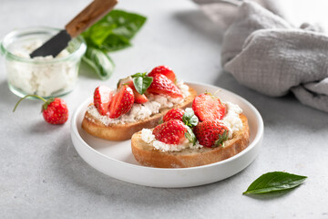 bruschettas with strawberries, cream cheese and basil in a white plate on a light background.