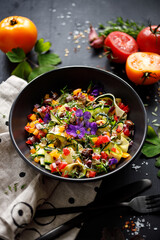Vegetarian salad with fresh vegetables and edible flowers in a black bowl top view