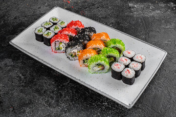 set of rolls and sushi on a white plate on a black textured background decorated with soy sauce and spices