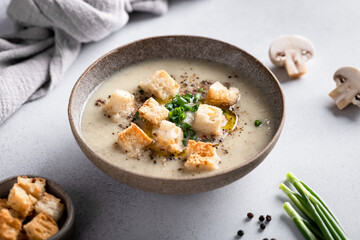mushroom cream soup with champignons and croutons in a ceramic bowl on a light background