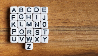 Set of 26 small white beads letters - whole alphabet - on wooden table, view from above, space for text right side