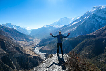 A man wearing a beanie and blue jumper, spreading his arms wide, breathing deeply the fresh...