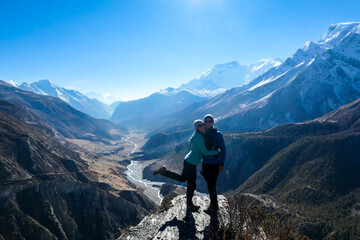 A couple standing at a mountain ledge, hugging and enjoying the view on Manang valley stretching in...