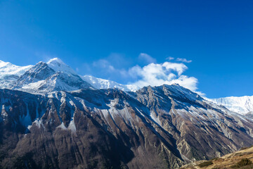 View on high Himalayas along Annapurna Circuit Trek, Nepal. Harsh and barren landscape around. Clear and blue sky. High Himalayan ranges around. Snow capped mountains. Serenity and calmness