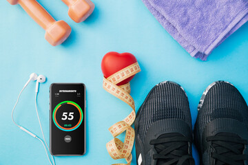 a top view of a red heart on a measure tape, a black phone with a chronometer , headphones , some masks,  a tape measure , dumbbells and shoes to workout at home