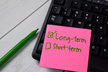Long-term and Short-term write on a sticky note. Supported by an additional services isolated wooden table.