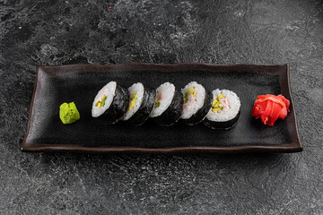 Sushi California Roll with crab meat, cucumber, masago, chopsticks on a gray plate, black background, side view