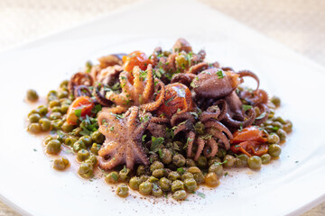 Octopus, peas and tomato. Ready to eat. Small octopuses cooked with cherry tomatoes, oil and peas. Tasty dish of Italian cuisine served on white plate.