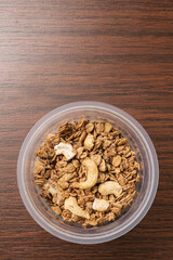 Top view of organic crunchy Granola Cereal with oats and cashew inside a plastic cup on wooden table. Ready to eat product, a nutrition snack for healthy, vegan, and dieting people.