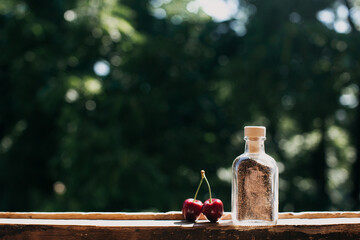 red cherries as notes, next to a small bottle with white sand on a green background. A summer picture with a summer Association. Inspiration for photographers. With space for text