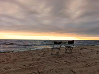 Two camp chairs with a fishing rod on the Bay in the sunset