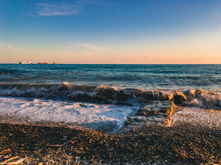 Fototapeta na wymiar A beautiful view of the Black Sea, waves with sea foam illuminated by the sunlight at sunset, run ashore with a breakwater against the blue sea on a sunny evening.