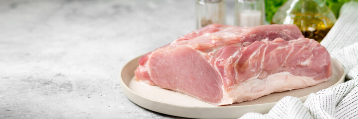 Raw pork carbonade on a wooden plate on the light gray kitchen table. Raw pork meat, tenderloin. Banner