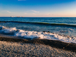 View of the Black Sea, waves with sea foam, lit by sunlight at sunset, run ashore against the blue sea on a sunny evening.