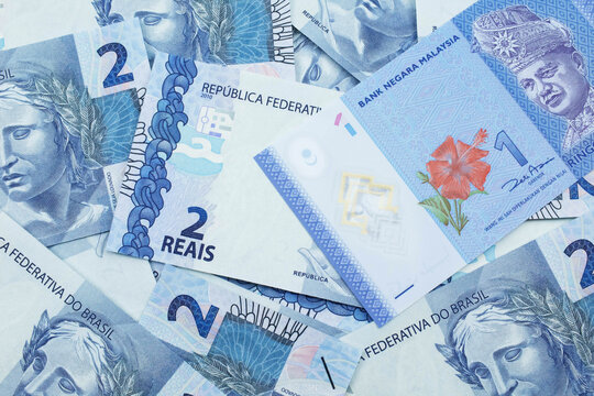 A close up image of a blue one Malaysian ringgit bank note on a bed of Brazilian two reais bank notes close up in macro