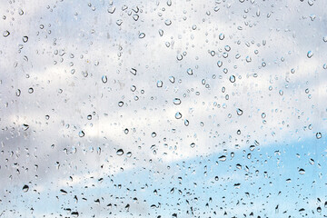 Raindrops on misted window glass against a blue sky.