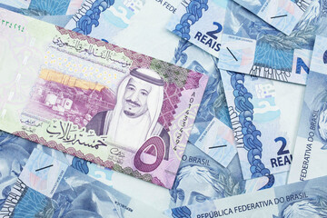 A close up image of a five riyal bank note from Saudi Arabia on a background of Brazilian two reais bank notes in macro