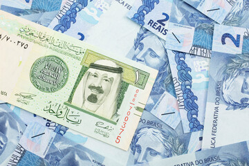A close up image of a one riyal bank note from Saudi Arabia on a background of Brazilian two reais bank notes in macro