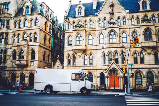 Van automobile driving on avenue in district with vintage buildings transporting goods for delivery service company, urban setting with oll historic architecture and traffic on road in district