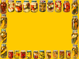 Frame from a variety of glass jars with canned vegetables on a yellow background.
