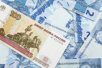 A close up image of a one hundred ruble bank note on a background of  Brazilian real notes from Mexico.  Shot close up in macro