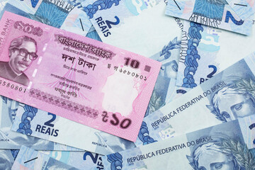 A close up image of a pink, ten taka bank note from Bangladesh on a bed of Brazilian two reais bank notes in macro