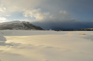 Fototapeta na wymiar blue sky over fjord and tromsoe city island and bridge with snow heavy clouds